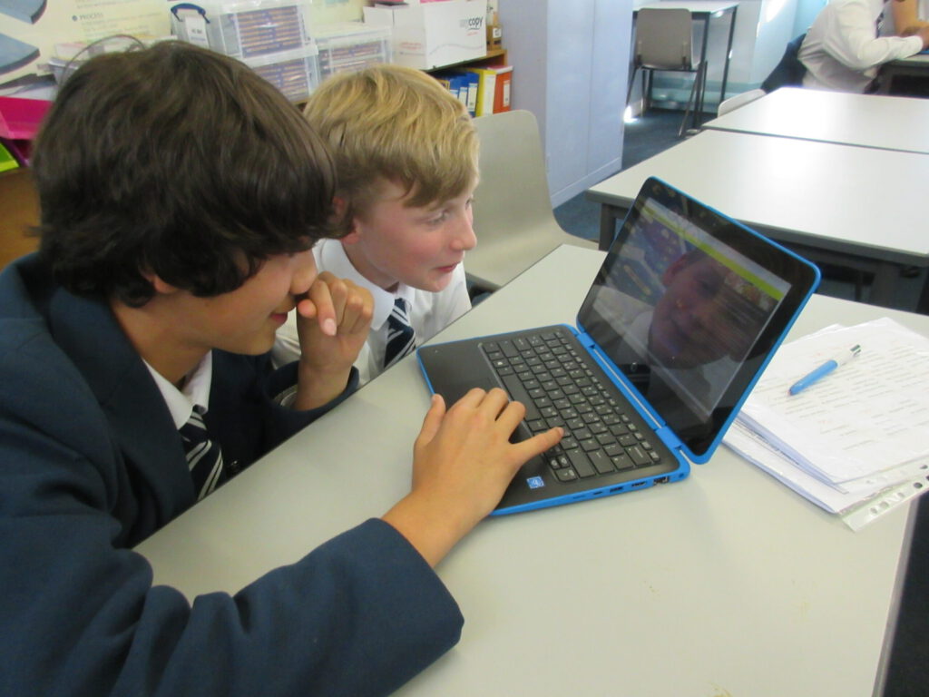 Two male pupils looking at stock market on laptop