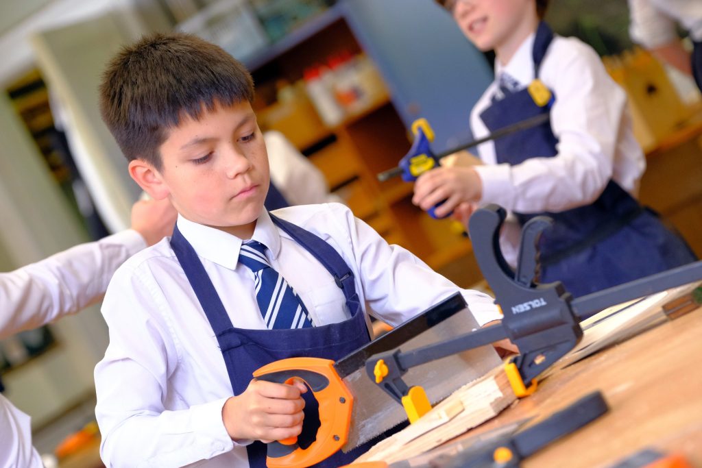 A pupil using a saw to cut a piece of wood