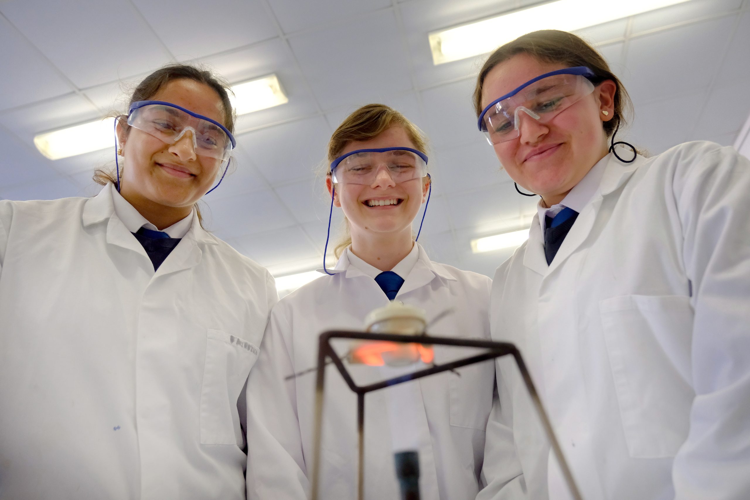 3 pupils smiling, dressed in lab coats