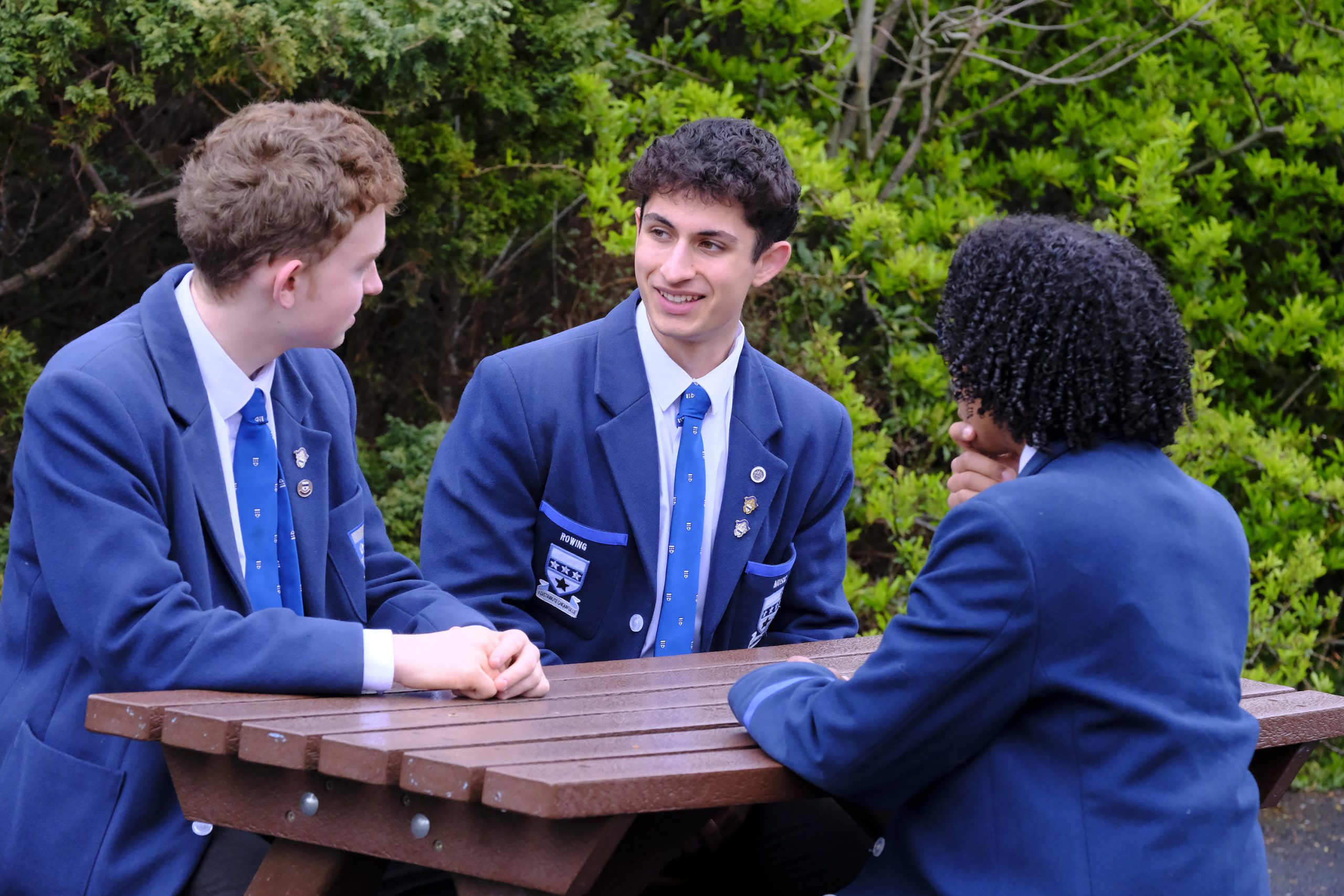 3 pupils sitting outside on a bench talking