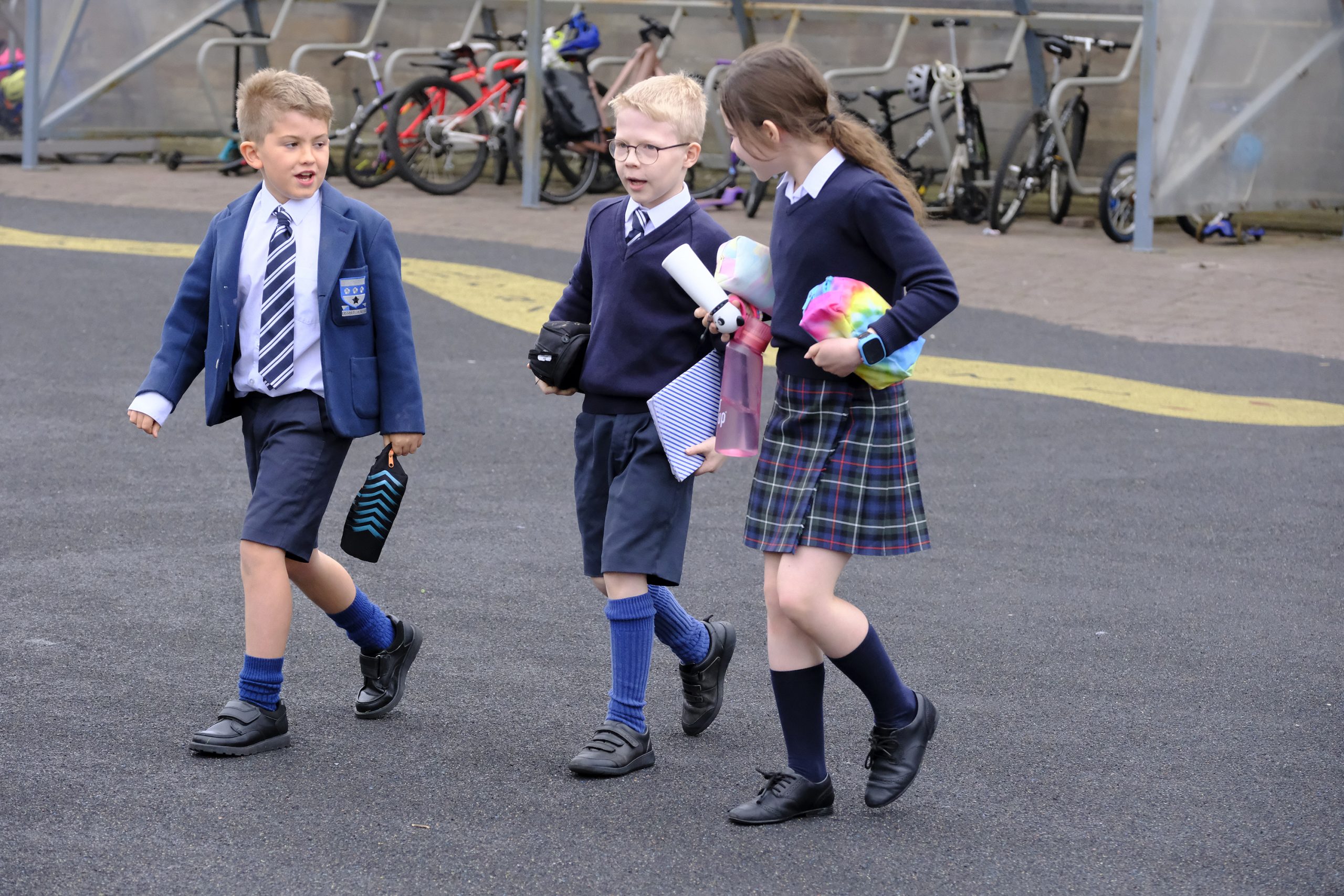 3 children holding school supplies, walking