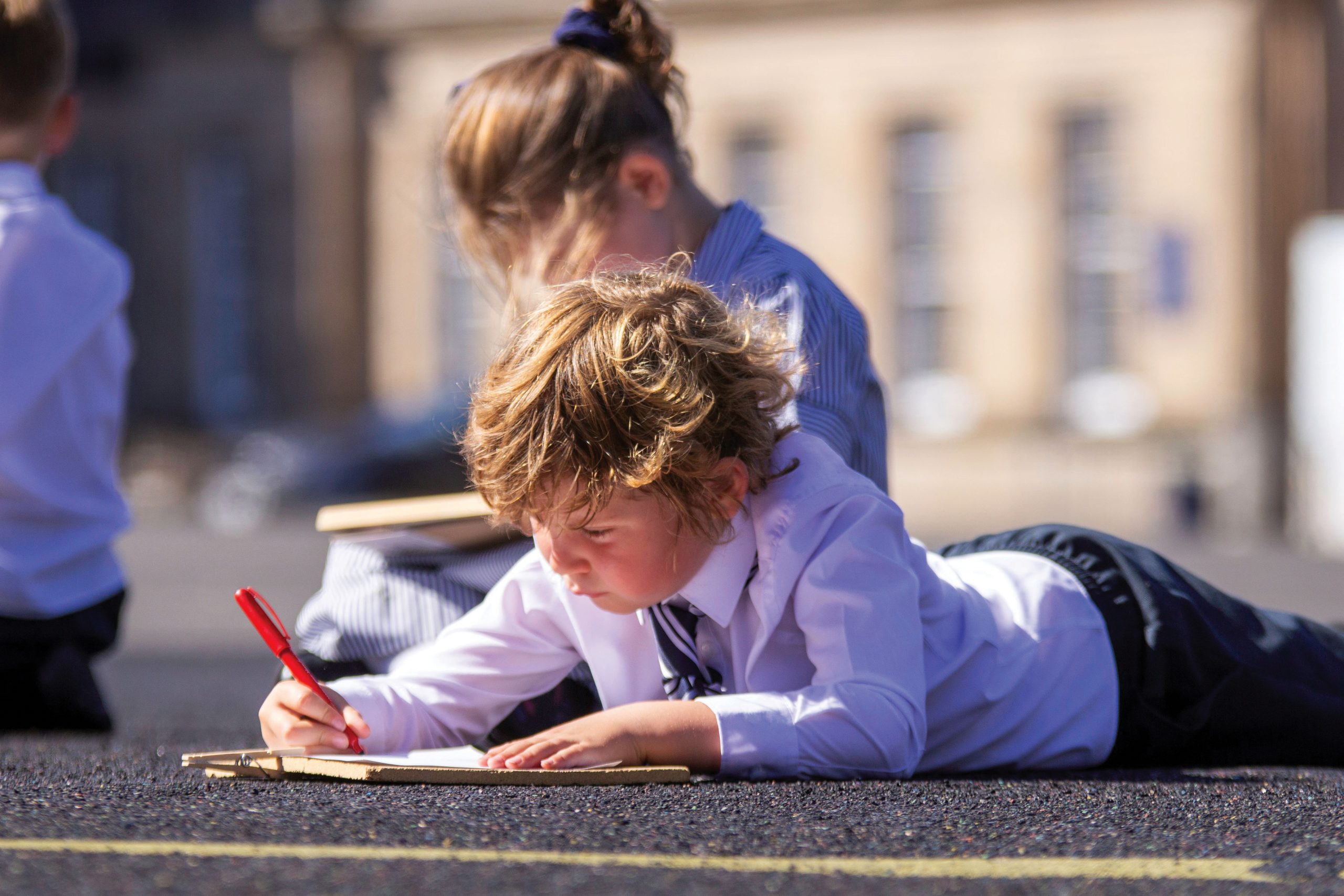 a boy lying on the ground outside writing