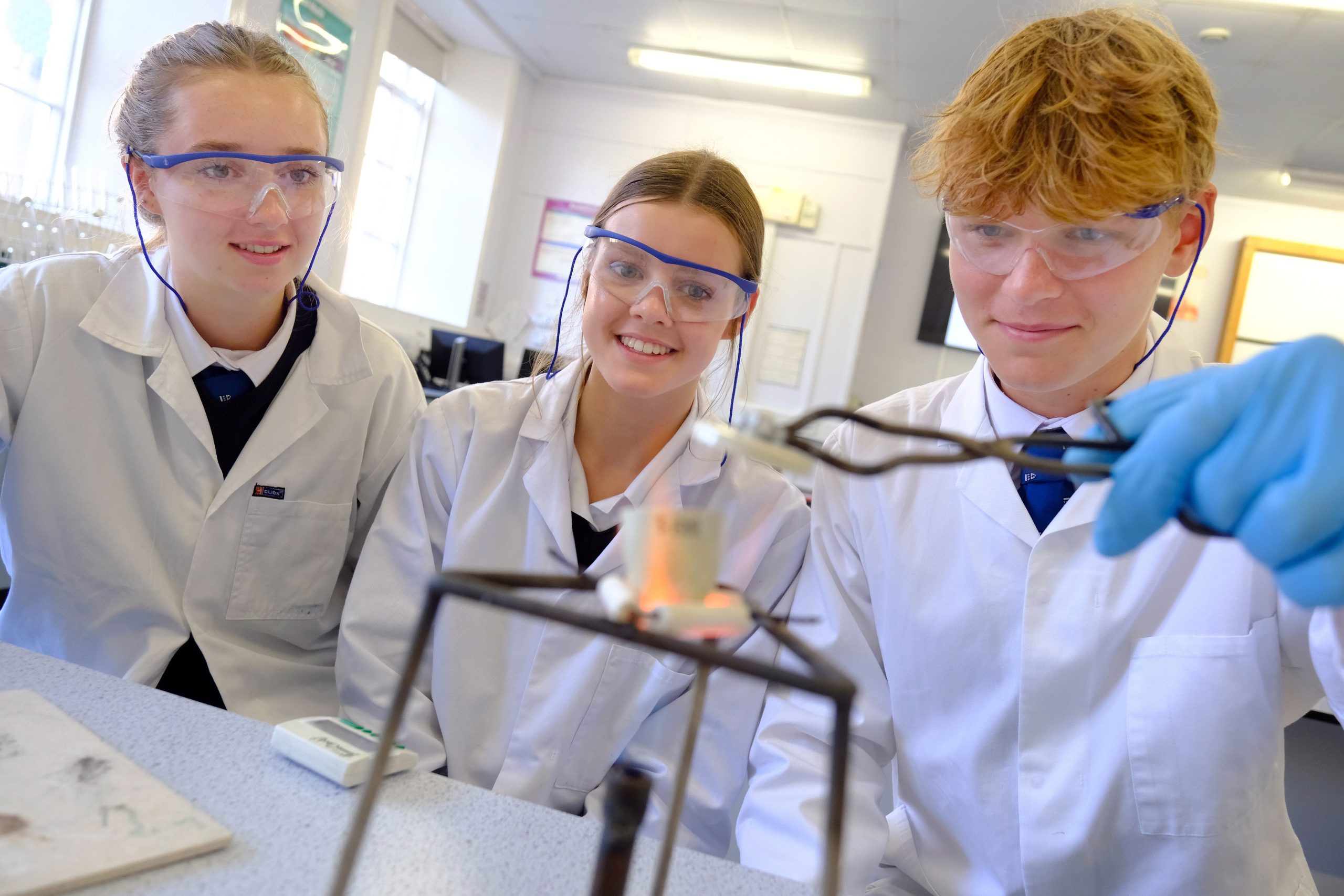 3 pupils in lab coats doing a science experiment