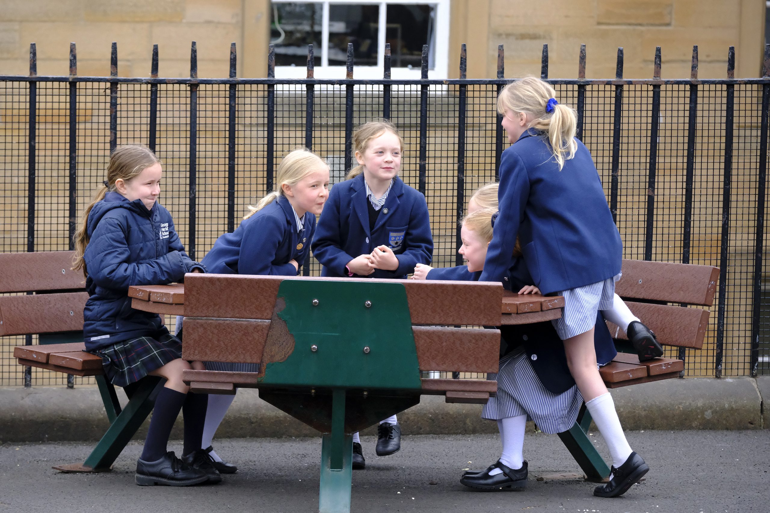 a group of girls sitting round a bench outside